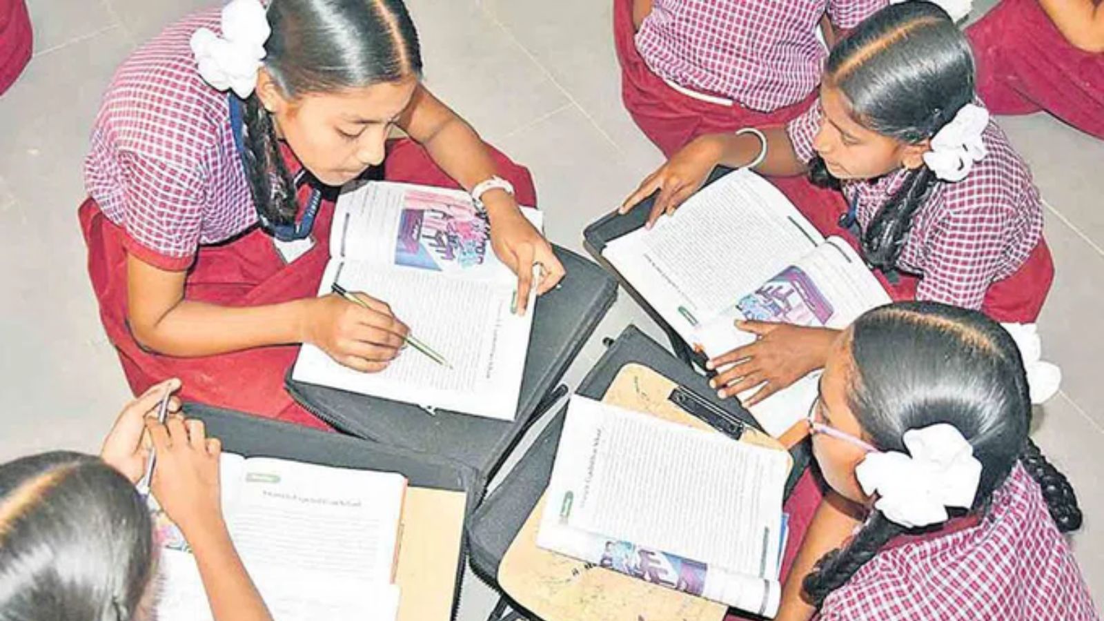 Image shows Young girls in school uniforms studying together on the floor with open textbooks.