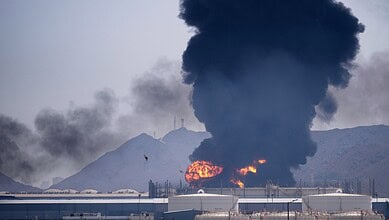 Fire and smoke at Fujairah oil storage facility after Iran's attack, with mountains in the background.