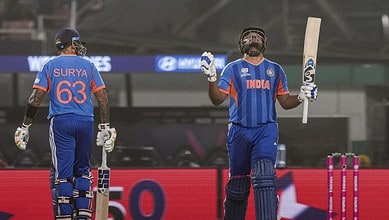 India players in blue jerseys, one raising bat in victory, stadium background.