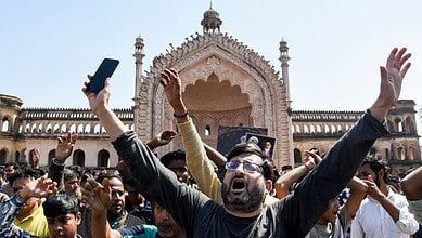 Crowd protesting in front of a historic building, raising hands and banners, amid political unrest.