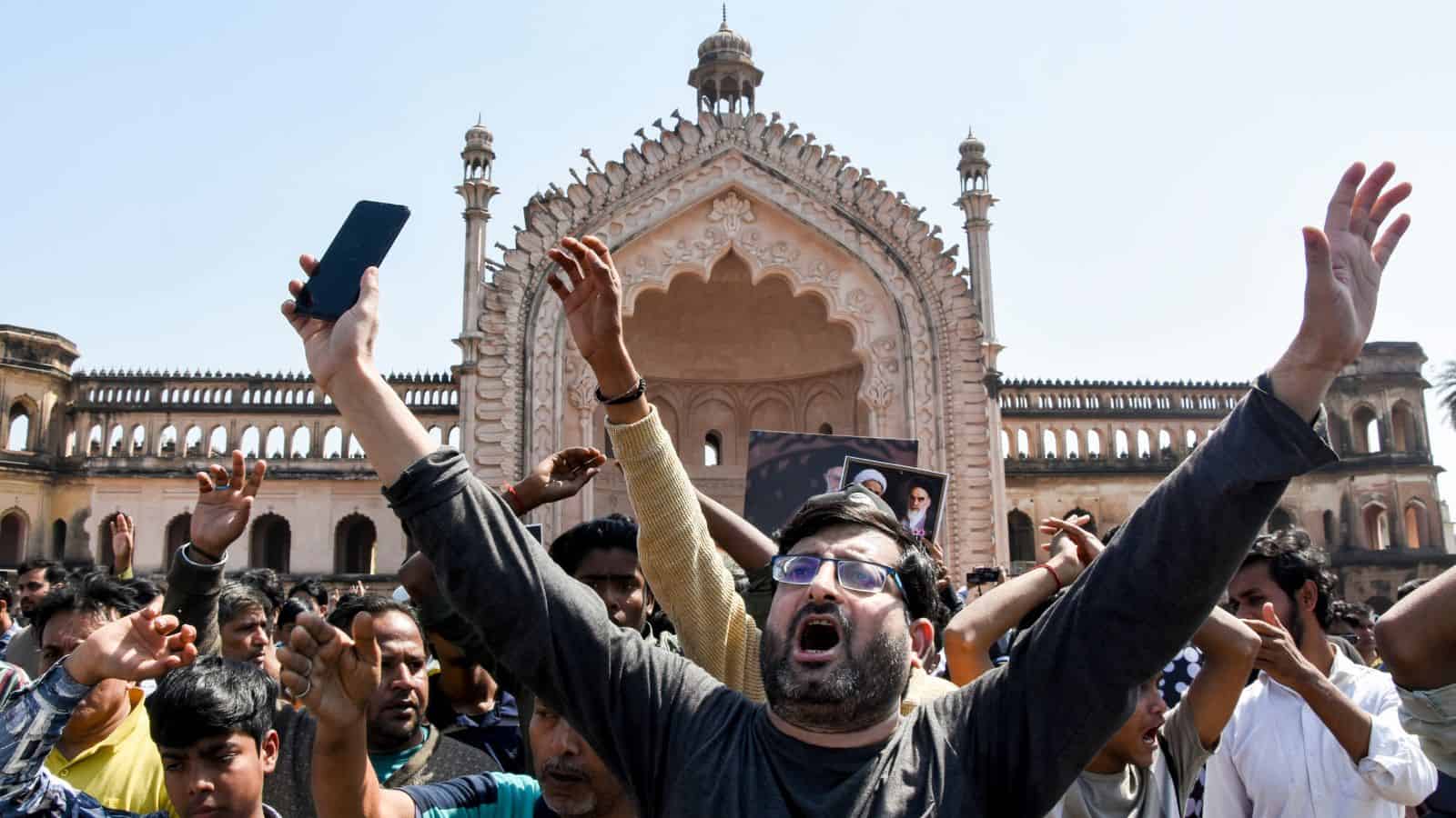 Crowd protesting in front of a historic building, raising hands and banners, amid political unrest.