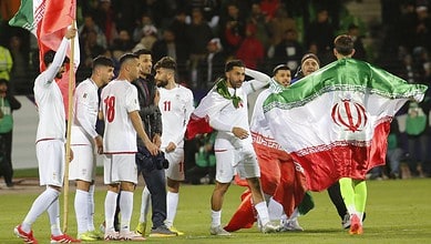 Iran football team with flag draped over players on the field.