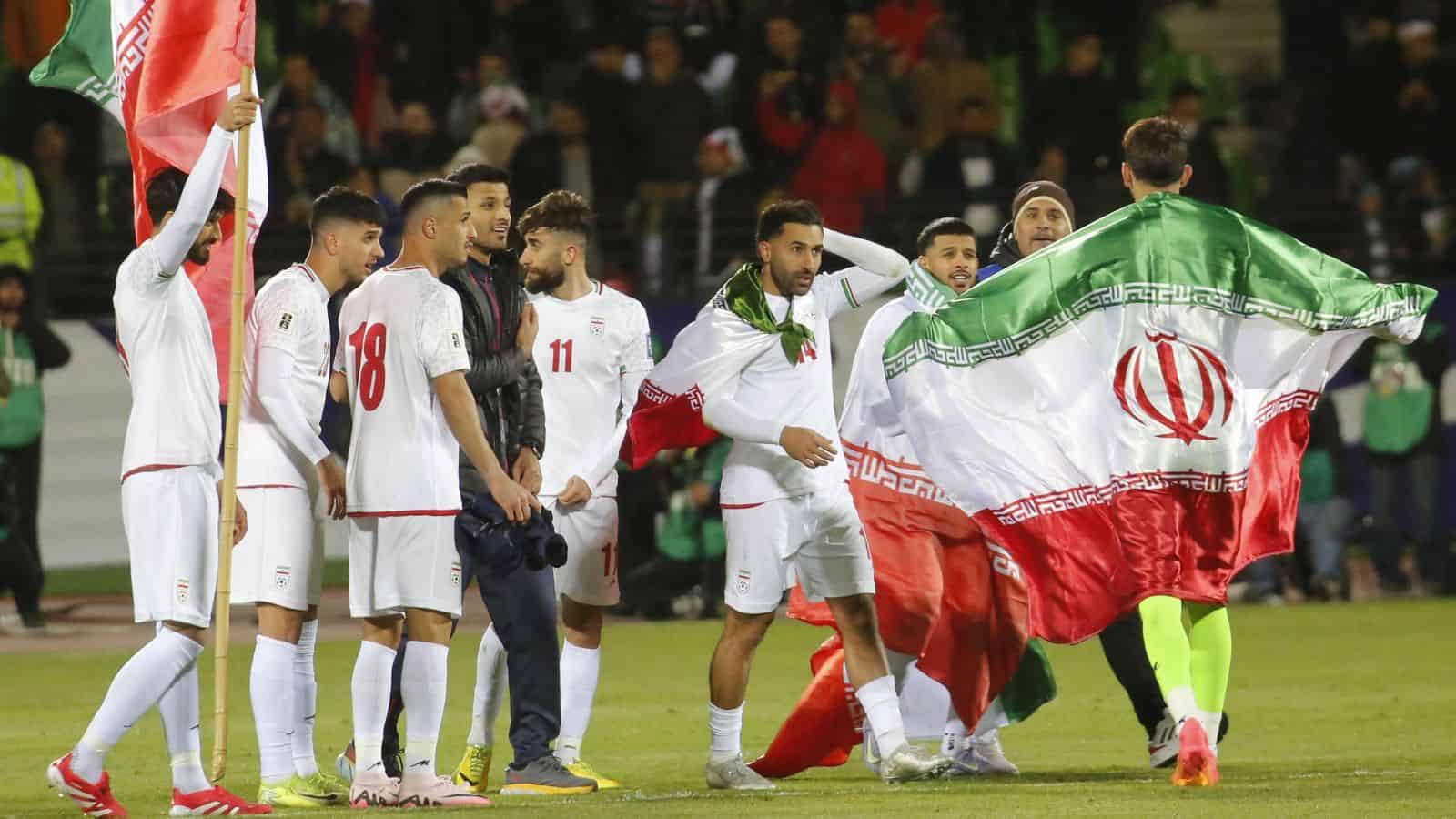 Iran football team with flag draped over players on the field.