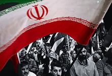 Iranian protesters waving flags in a defiant rally against US and Israel.