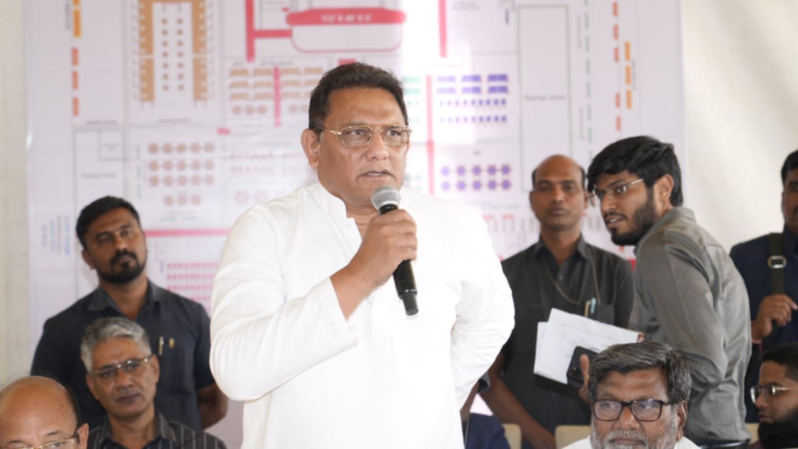 A political leader addressing the media during a press conference with journalists and staff present.