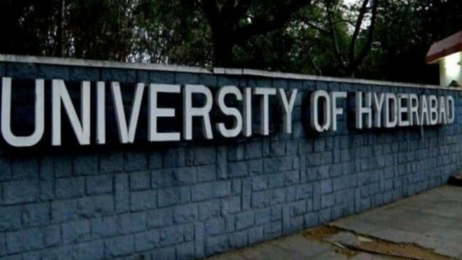 University of Hyderabad signboard with campus trees in background.