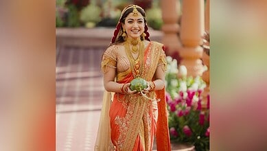 Rashmika Mandana dressed in vibrant traditional Indian attire, smiling and holding a decorative item duri.