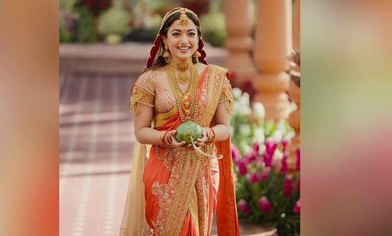 Rashmika Mandana dressed in vibrant traditional Indian attire, smiling and holding a decorative item duri.