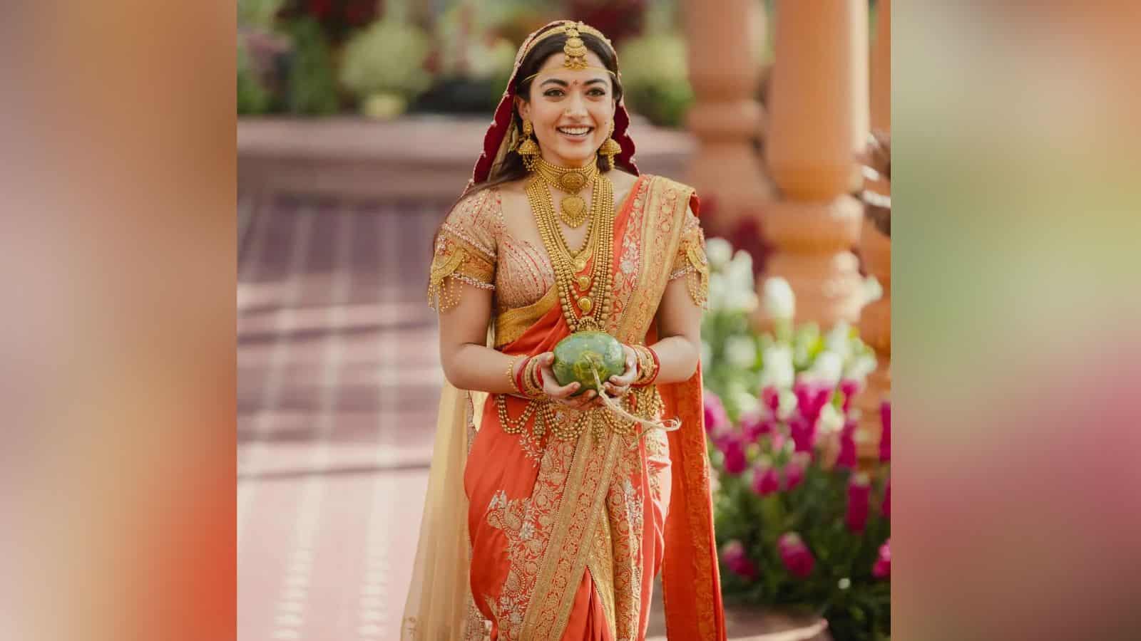 Rashmika Mandana dressed in vibrant traditional Indian attire, smiling and holding a decorative item duri.