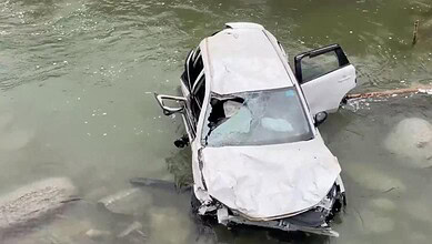 Car submerged in stream after accident, with visible damage.