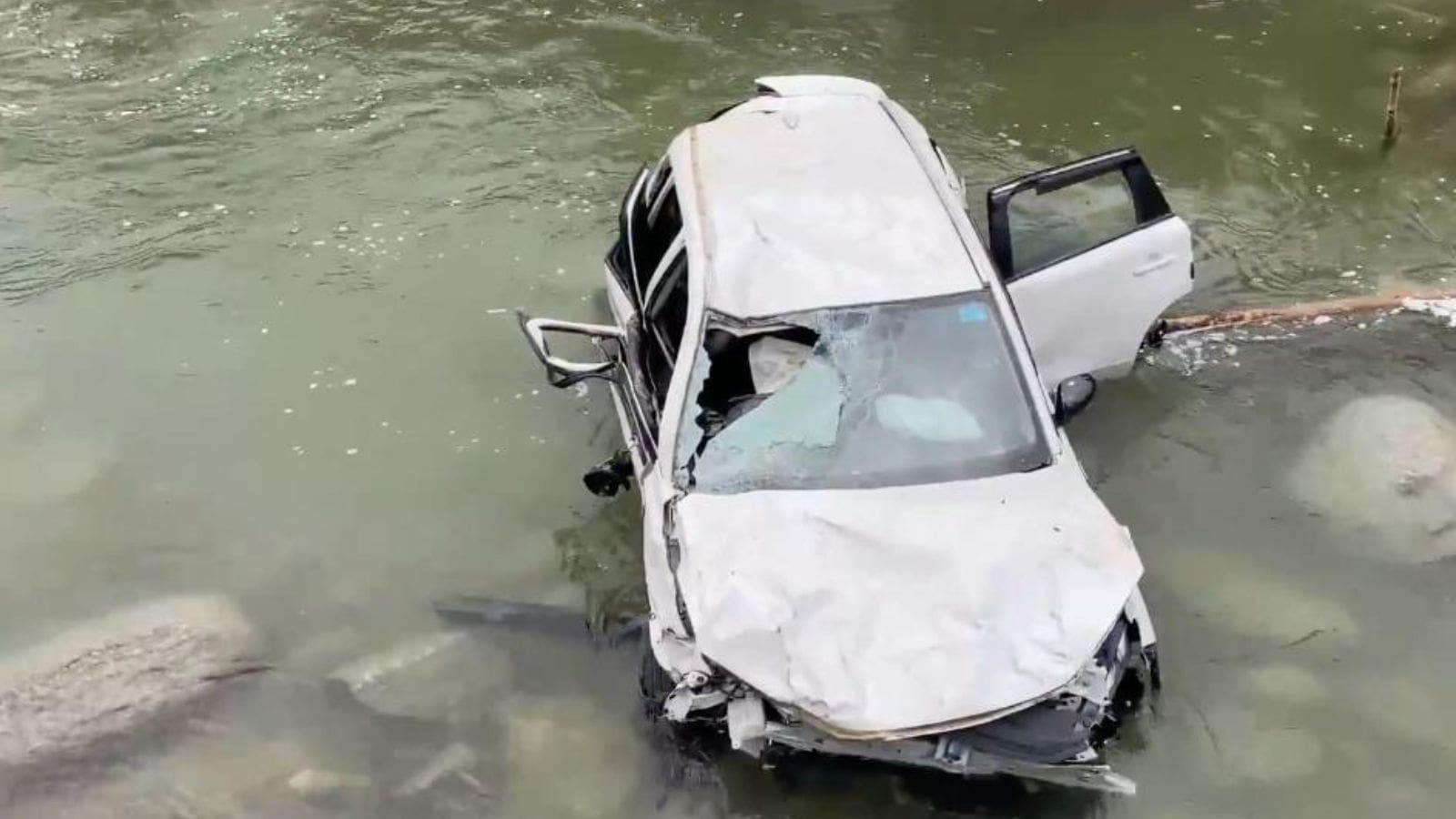 Car submerged in stream after accident, with visible damage.