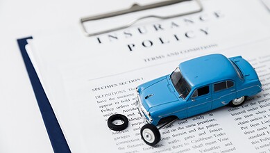 Car insurance policy document with a toy car and a tire on top.