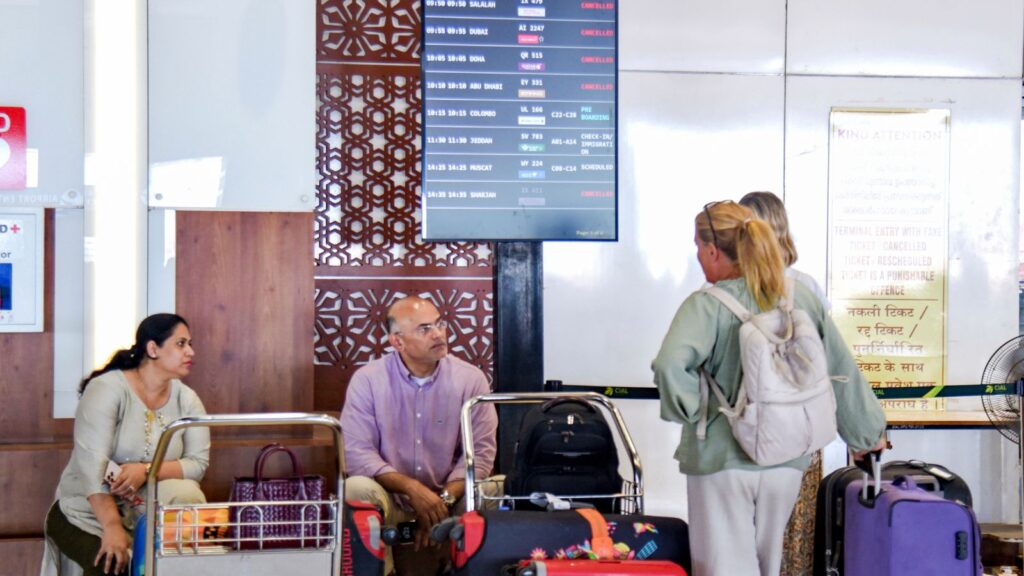 Passengers at an airport check flight cancellations on digital screens during international travel disrup.