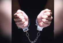 Close-up of two clenched fists bound together by silver metal handcuffs against a dark background.
