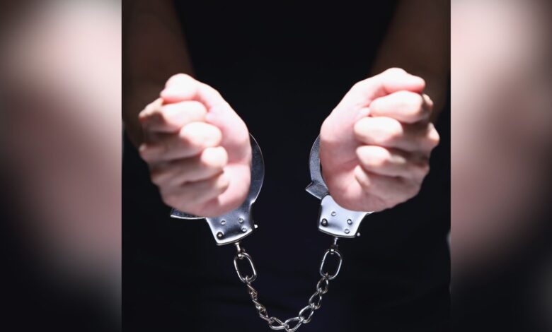 Close-up of two clenched fists bound together by silver metal handcuffs against a dark background.