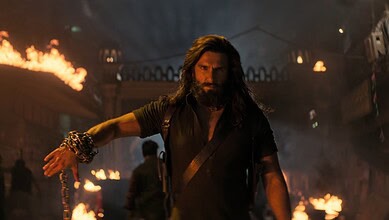 A dramatic scene from the Dhurandhar 2 trailer featuring a intense male character amidst fire and chaos.