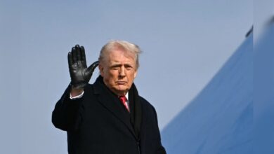 Donald Trump waves while wearing a black coat and gloves.