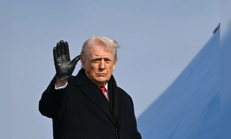 Donald Trump waves while wearing a black coat and gloves.