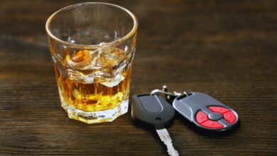 Image shows A glass of whiskey on the rocks beside car keys on a wooden surface.