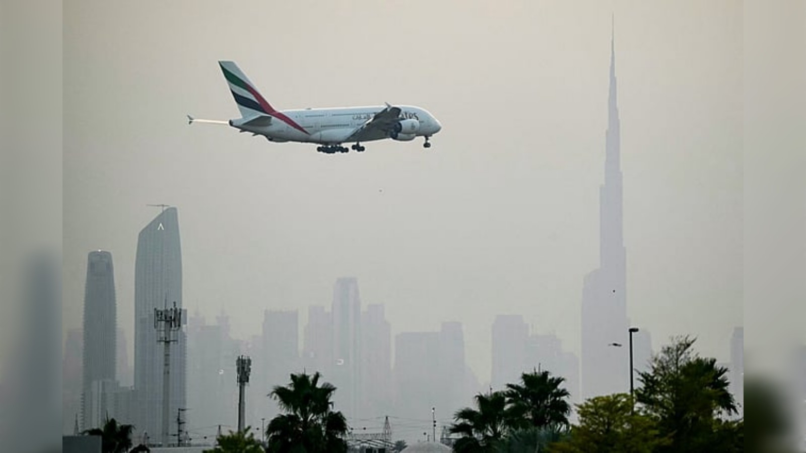 Emirates Airbus A380 approaching landing at Dubai International Airport with Dubai skyline and Burj Khalifa in the background.