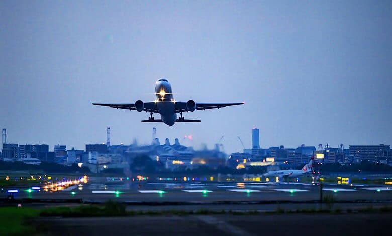 Airplane taking off from runway at dusk, with city skyline in background.