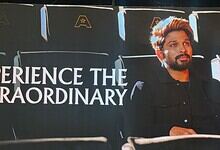 A man sitting in a cinema theatre with a backdrop displaying "Experience the Extraordinary" at Allu Cinem.