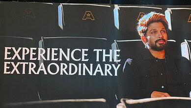 A man sitting in a cinema theatre with a backdrop displaying "Experience the Extraordinary" at Allu Cinem.