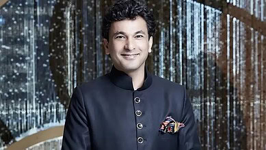 Vikas Khanna, renowned chef, smiling at a culinary event with a backdrop of shimmering lights.