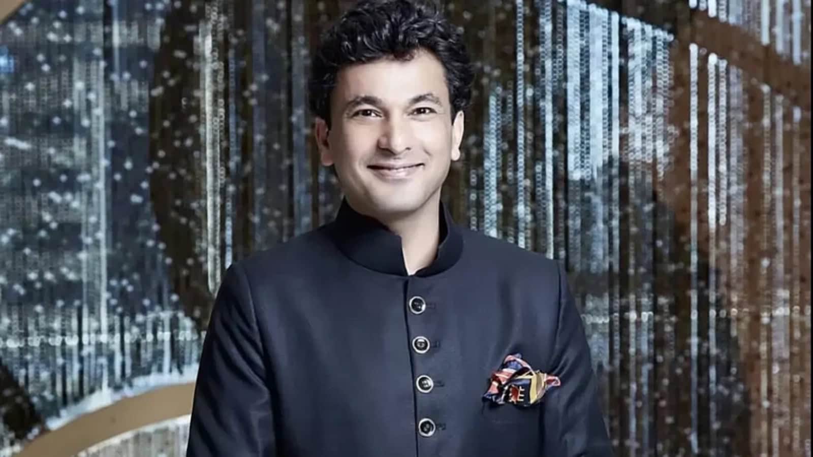 Vikas Khanna, renowned chef, smiling at a culinary event with a backdrop of shimmering lights.