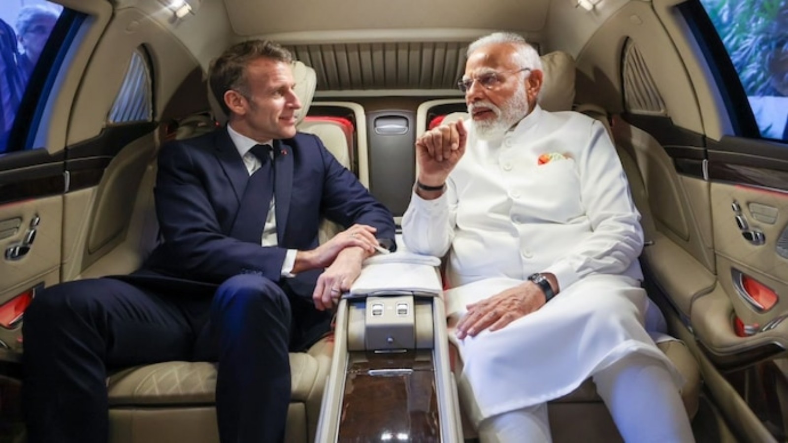 Indian Prime Minister Narendra Modi and French President Emmanuel Macron seated inside an car, engaged in conversation.