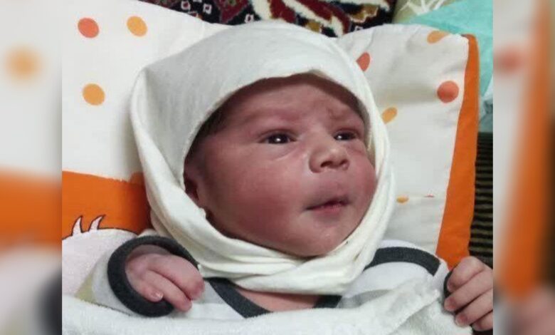 Newborn baby Mojtaba wrapped in a white cloth, lying on a patterned cushion.