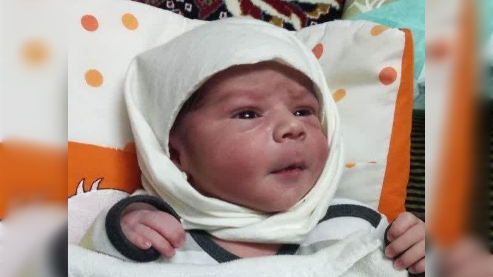 Newborn baby Mojtaba wrapped in a white cloth, lying on a patterned cushion.
