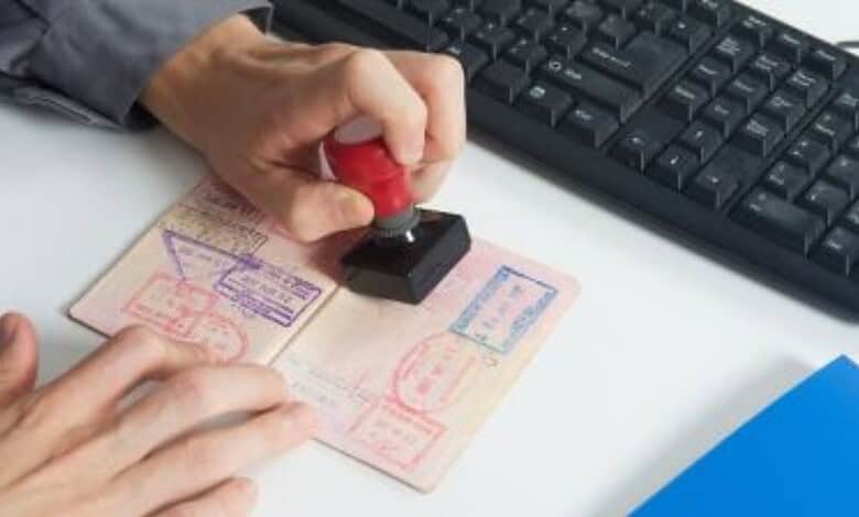 Hand stamping a passport document on a desk beside a computer keyboard.