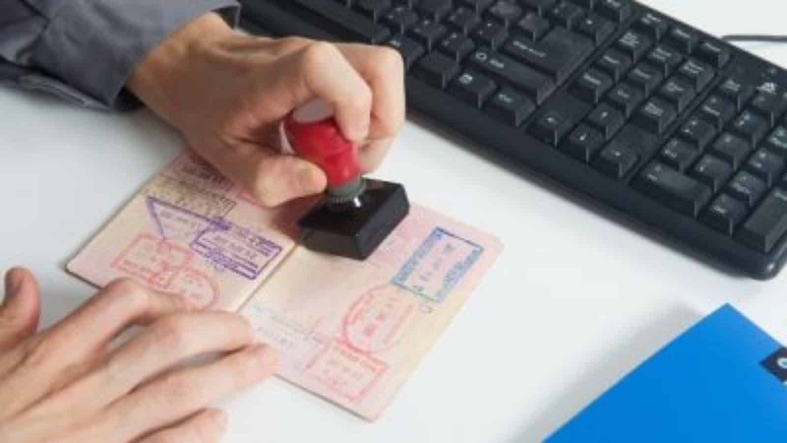Hand stamping a passport document on a desk beside a computer keyboard.