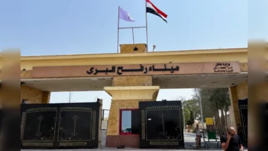 Egyptian side of Rafah border crossing gate with flags and security post.