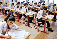Students sit in a classroom writing board examinations at their desks.