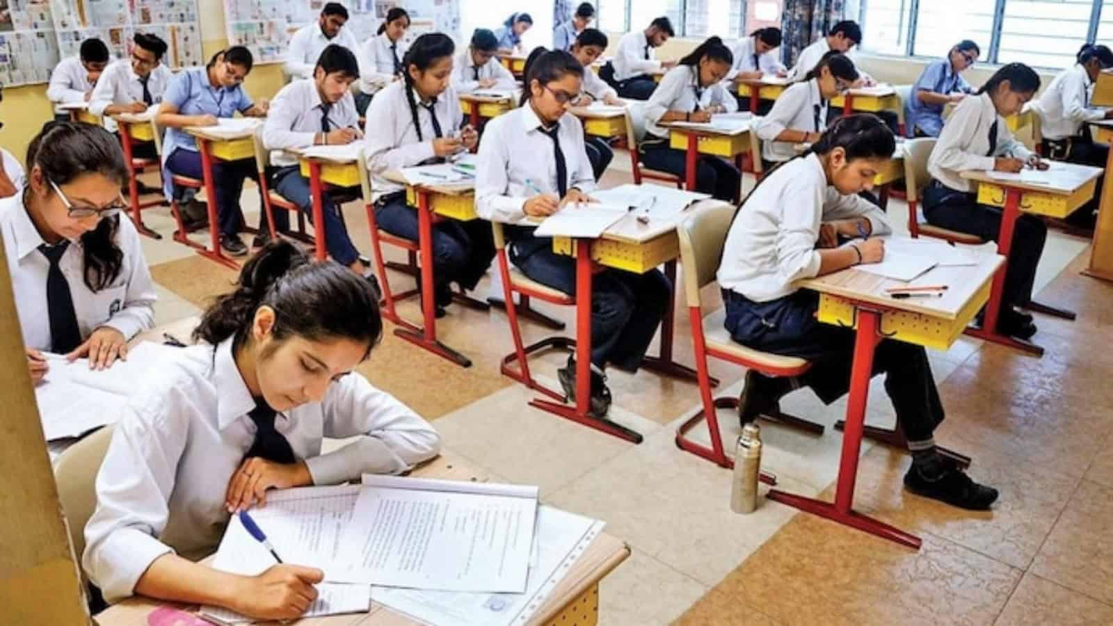 Students sit in a classroom writing board examinations at their desks.