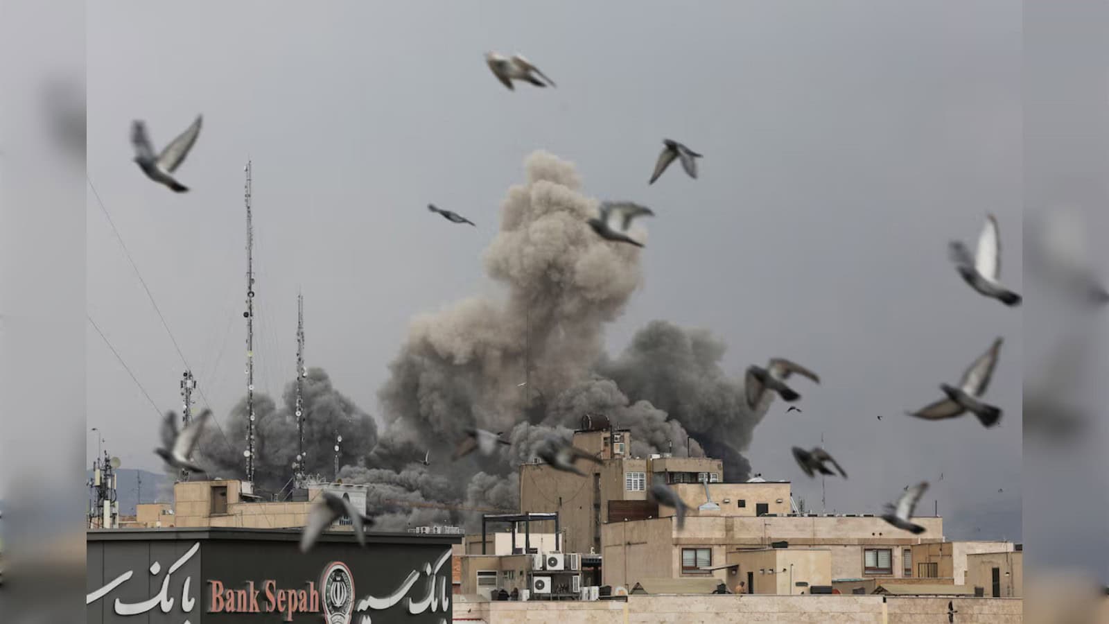 Birds fly over buildings in Tehran as a large plume of smoke rises following explosions during US and Israeli strikes on Iran.