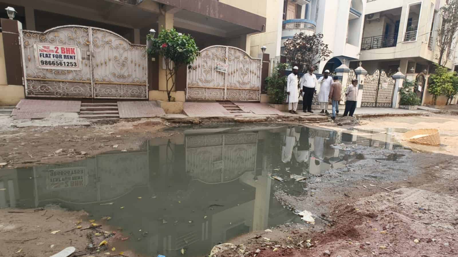 Flooded street with dug-up roads and residents raising alarm in Tolichowki.