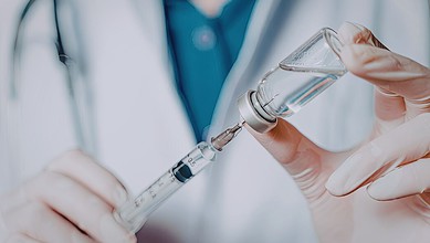Image shows a healthcare worker drawing vaccine into a syringe, highlighting Covid vaccine administration and related policies.