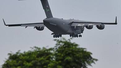 Military cargo plane in flight over trees during overcast weather.