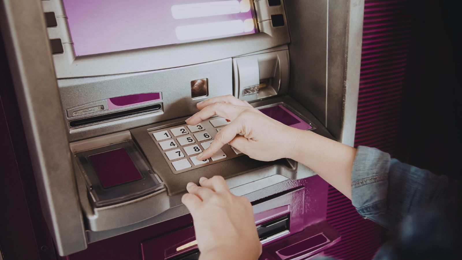 Image shows Person entering PIN on an ATM keypad