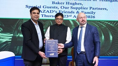 Three men at a formal event, one holding a certificate, with a digital screen in the background.