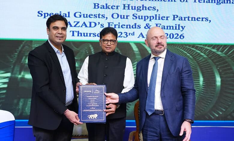 Three men at a formal event, one holding a certificate, with a digital screen in the background.