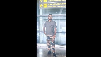 Man posing as CISF officer at Hyderabad airport, taking photos, with airport signage in background.