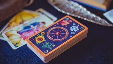 Tarot card deck with colourful designs on a table, surrounded by tarot cards and crystals.