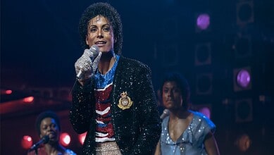 Actress portraying Michael Jackson in a biopic performs on stage with microphone, dressed in iconic style.