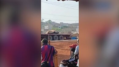 Explosion site in Mali with military vehicles and civilians nearby.