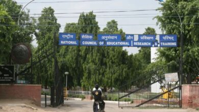 Image shows NCERT headquarters entrance gate with blue signboard displaying the organization's name in Hindi and English.