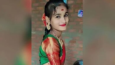 Young girl dressed in colourful traditional clothes, smiling, with a brick wall background.